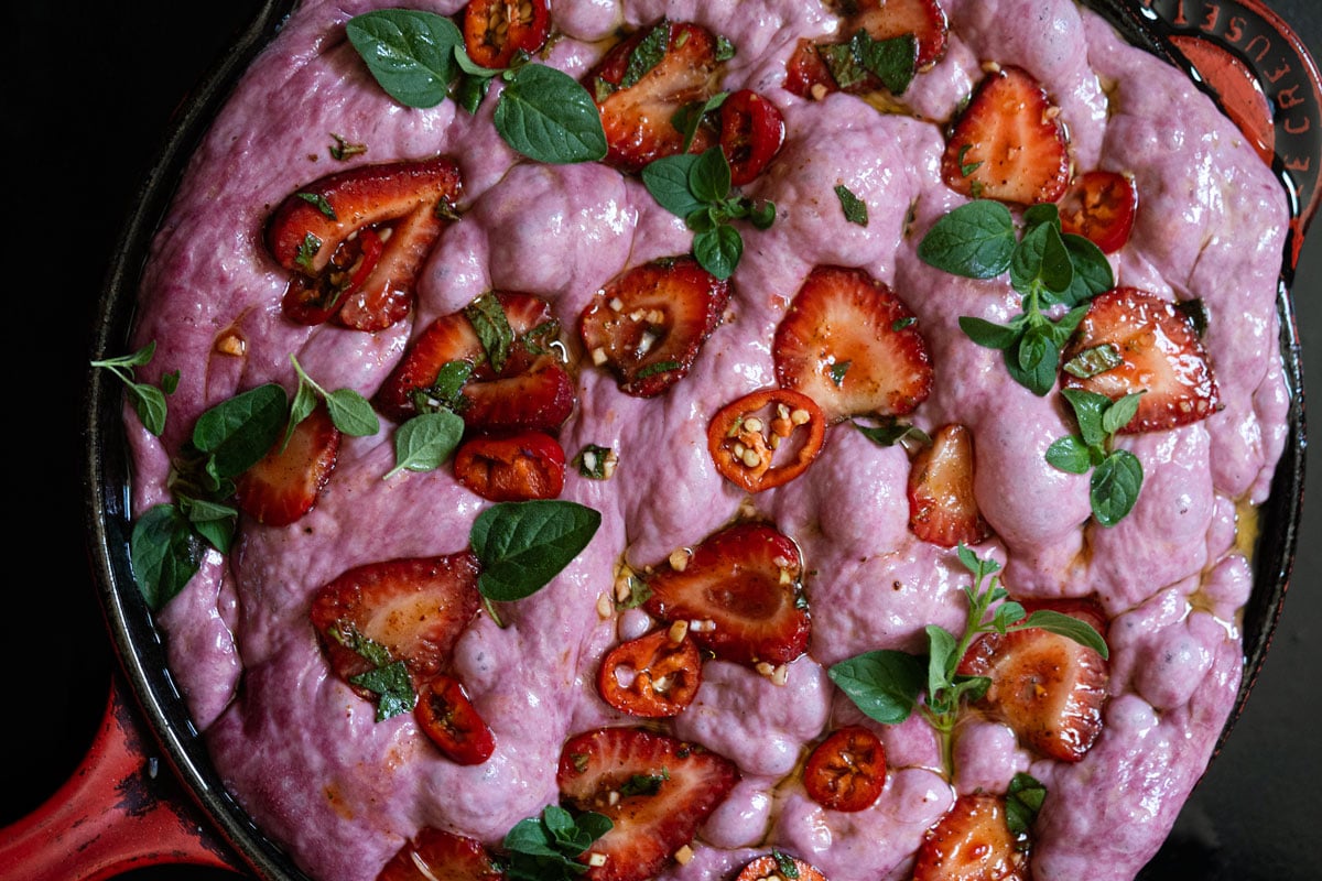 Unbaked sourdough strawberry focaccia in a skillet topped with strawberry and chipotle slices
